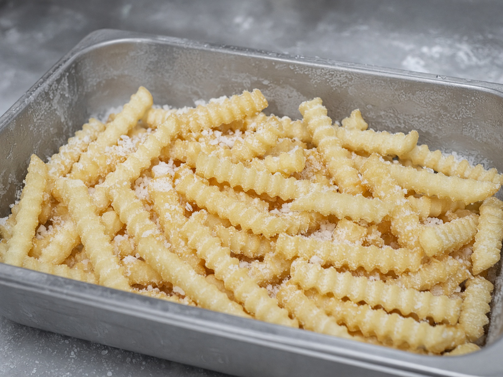 Frozen par-fried straight-cut and crinkle french fries on a steel tray.
